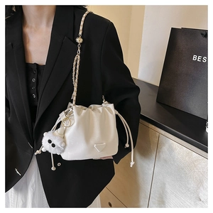 Detail of white glossy drawstring bucket bag with gold chain strap and plush ball charm