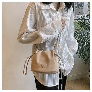 Detail of beige suede drawstring bucket bag with gold chain strap worn by a model