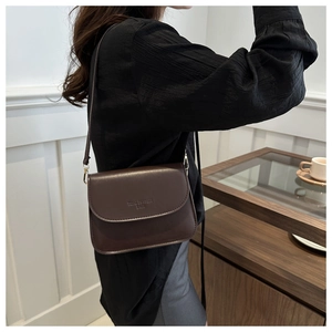 Détail d'un petit sac carré marron foncé avec logo embossé et boucles en métal doré