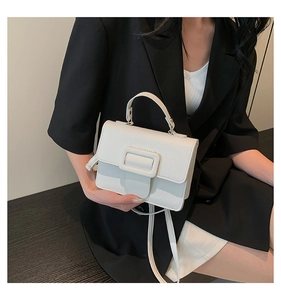 Détail du petit sac blanc en cuir grainé avec boucle décorative porté sur une veste noire