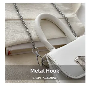 Close-up of silver metal hardware hook and litchi texture leather detail on white mini bag