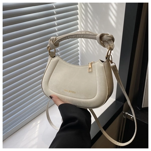 Detail of cream saddle bag featuring a unique twisted handle and gold zipper closure