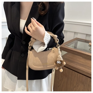 Close-up of beige leather handbag with knotted handle and plush monster charm detail