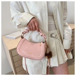Pink crescent handbag with knotted handle and plush charm detail on a white outfit