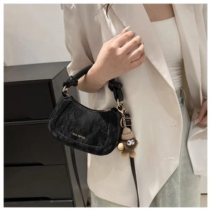 Detail of black faux leather bag with marble texture and plush doll charm