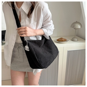 Detail of black corduroy tote bag featuring a cute cartoon pendant and wide shoulder strap