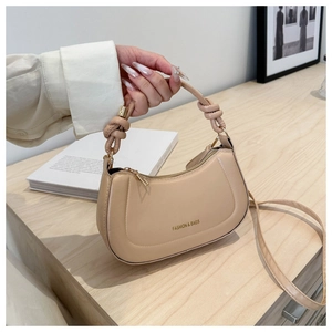 Detail of a beige crescent hobo bag with unique knotted handle and gold fashion lettering