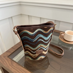 Retro wavy knit bucket bag with brown leather strap displayed on a wooden table