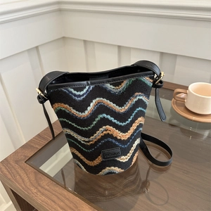 Fashion bucket bag with colorful wave embroidery and black leather strap on a table