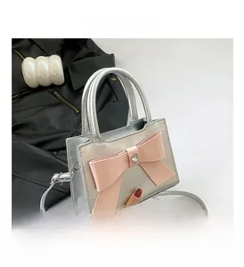 Détail d'un sac à main en cuir verni argenté avec nœud rose et pierre en forme de cœur