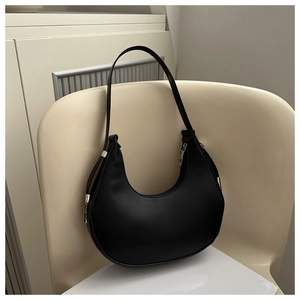 Detailed side view of black matte leather crescent bag with silver zipper on a wooden chair