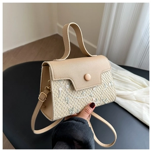 Close-up of woven straw handbag featuring floral embroidery and beige PU leather flap