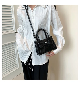 Détail d'un petit sac en cuir verni noir avec un grand nœud et cristal en cœur