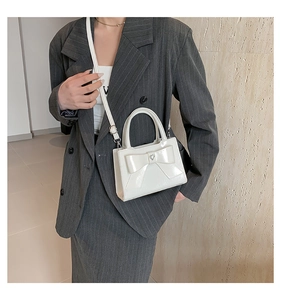 Détail du sac à main blanc à nœud avec boucle en cœur et finition en cuir verni brillant