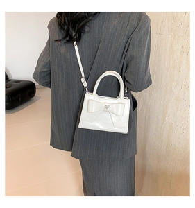 Détail d'un sac à main blanc avec nœud papillon porté par un mannequin en costume gris