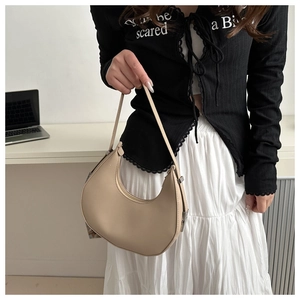 Close-up of a minimalist beige crescent underarm bag worn by a model in a modern office setting