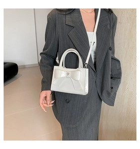 Detail of white patent leather handbag with large bow and heart metal charm decoration