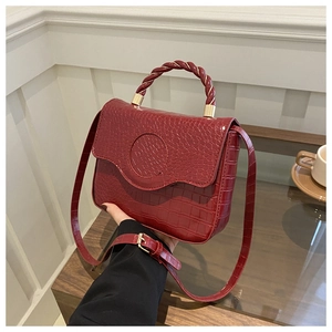 Macro detail of wine red crocodile embossed leather and braided handle on handbag
