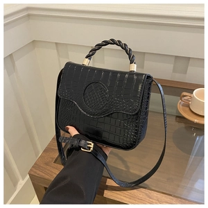Detail of black crocodile texture handbag with unique twisted handle and gold hardware