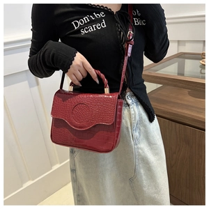 Detail of wine red faux crocodile skin handbag with woven handle and gold-tone hardware