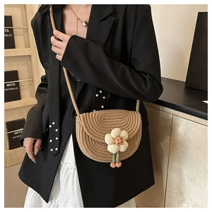 Detail of woven saddle bag featuring 3D floral accent and natural straw texture finish