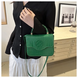 Detail showing high-quality green crocodile pattern texture and round decorative clasp on handbag