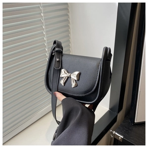 Détail d'un sac selle noir mat avec un nœud argenté miroir et une bandoulière en cuir