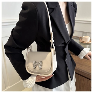 Detail of elegant cream leather saddle bag featuring a silver bow buckle and shoulder strap