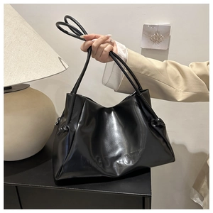 Detail of black faux leather tote bag showing side knot and embossed logo on the bottom