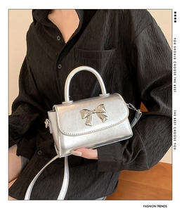 Detail of silver metallic crossbody bag with bow buckle and textured leather finish
