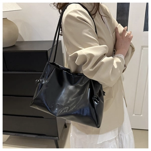 Detail of a black ruched tote bag featuring drawstring knots and glossy PU leather finish