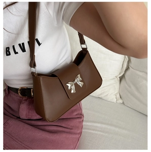 Detail of a brown leather shoulder bag featuring a silver metal bow buckle clasp