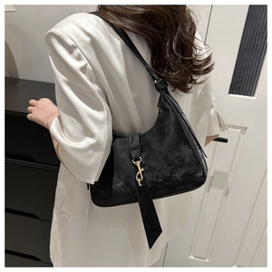 Detail of a black crescent shoulder bag with golden metallic clasp on a white silk blazer