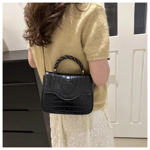 Detail of black croc-effect small square bag with unique twisted woven top handle
