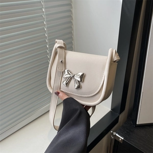 Cream leather saddle crossbody bag featuring a silver bow buckle and adjustable strap