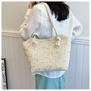 Detail of woven straw tote bag featuring floral embroidery and thick rope shoulder straps
