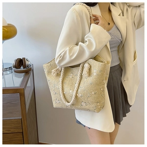 Detail of a woven straw tote bag with floral embroidery and cotton rope handles