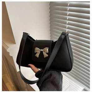 Close-up of matte black shoulder bag featuring a prominent silver metal bow buckle