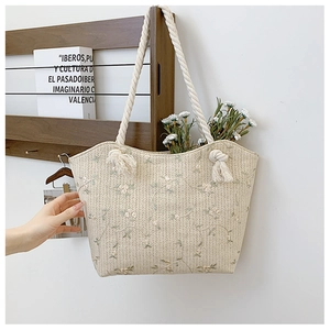 Detail of light beige straw tote bag featuring green floral embroidery and cotton rope handles