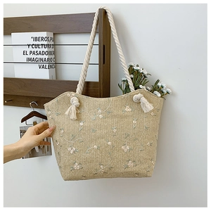 Detail of straw tote bag with floral embroidery and braided rope handle on wooden rack