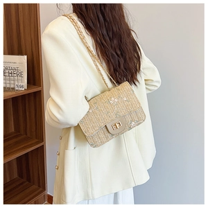 Detail of light beige straw saddle bag with floral embroidery and gold chain strap