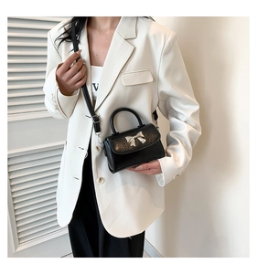 Detail of a black leather mini handbag with a silver metal bow buckle on white blazer