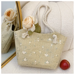 Detail of light green straw tote featuring floral embroidery and knotted hemp rope handles