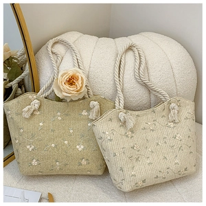 Detail of straw woven tote bags with white floral embroidery and cotton rope handles