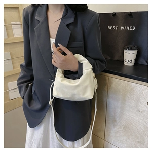 Detail of elegant pleated cream crossbody bag with a designer metal charm and leather strap