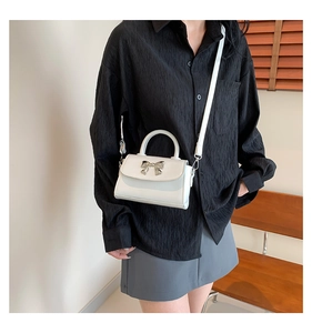 Detail of white mini crossbody bag featuring a silver metal bow accent and leather texture