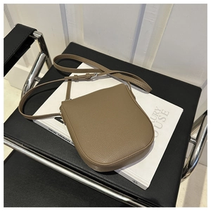 Detail of khaki pebbled leather crossbody bag on a book showing texture and silver hardware