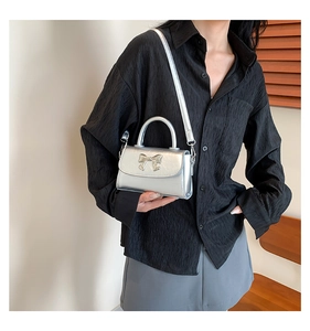 Detail of silver metallic mini bag featuring a stylish bow ornament and smooth handle