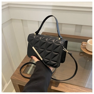 Detail of black quilted handbag with gold metal trim and leather top handle