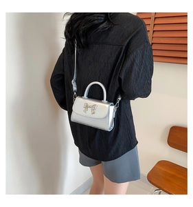 Detail of silver metallic mini bag featuring a chic bow accent and slim crossbody strap